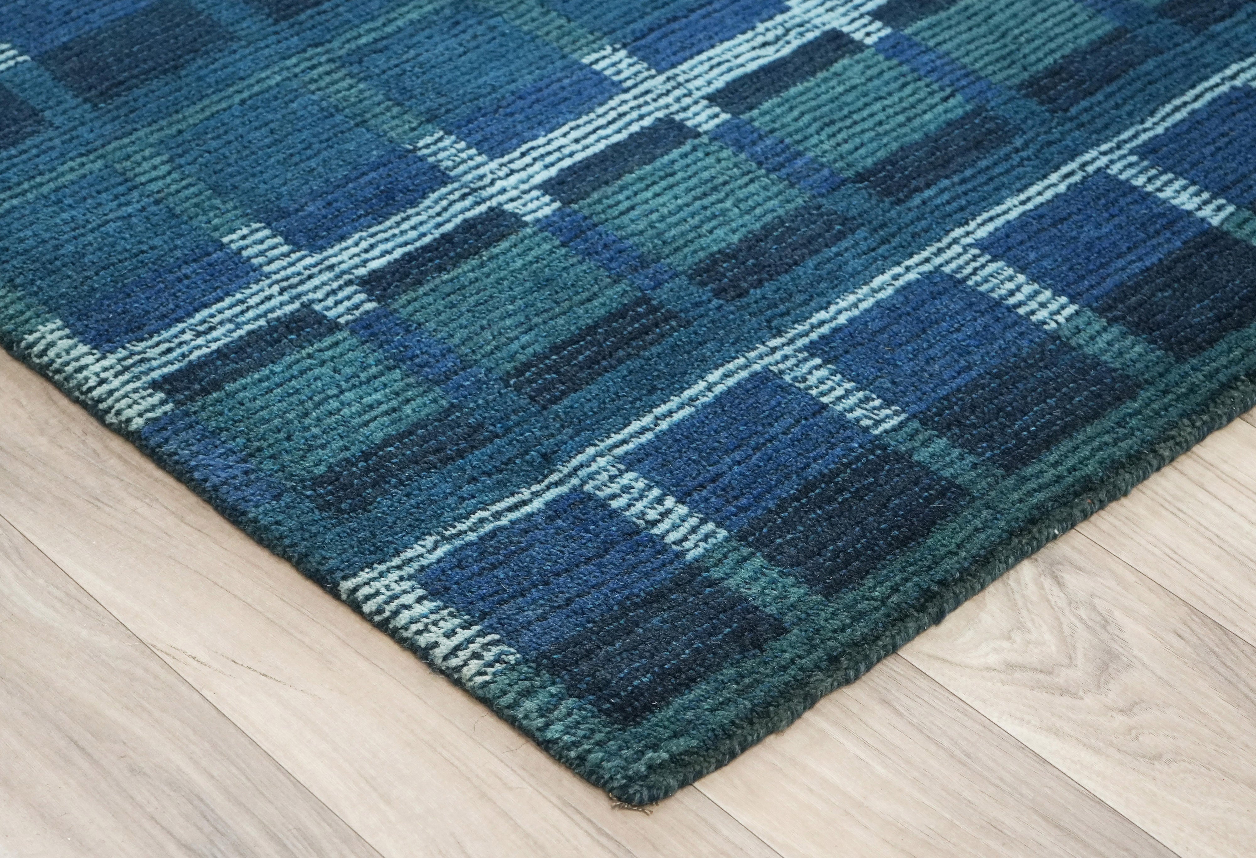 Corner detail of Lagoon Lattice blue wool hand tufted rug on light wooden floor.