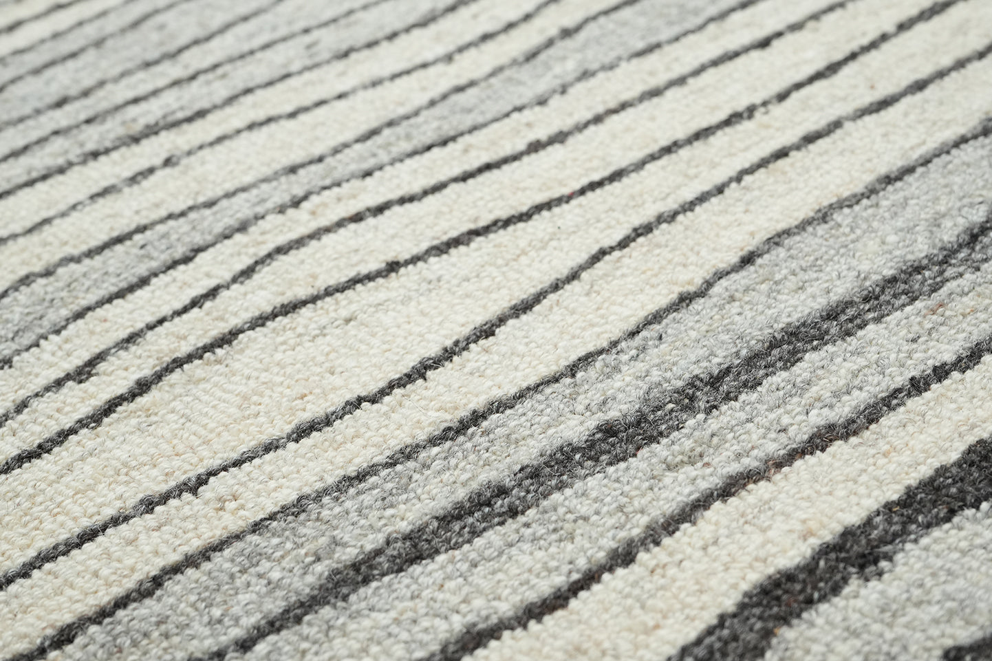 Lithos hand tufted wool rug shown in close up detailing the textured pile and flowing linear pattern in grey shades.