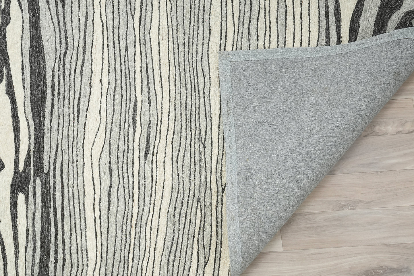 Lithos hand tufted wool rug showing a folded corner with the backing visible and the layered line pattern on the surface