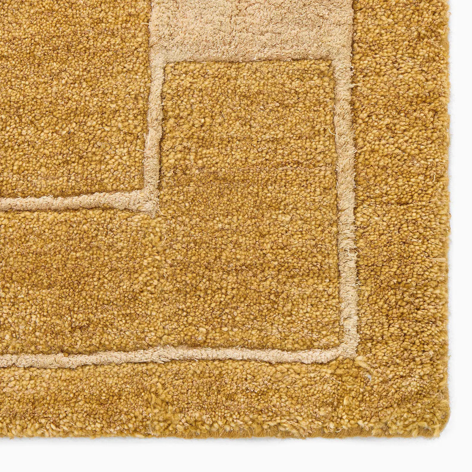 Close-up of an ochre color mid-century modern hand tufted rug showing a textured surface and stitched geometric border detail.