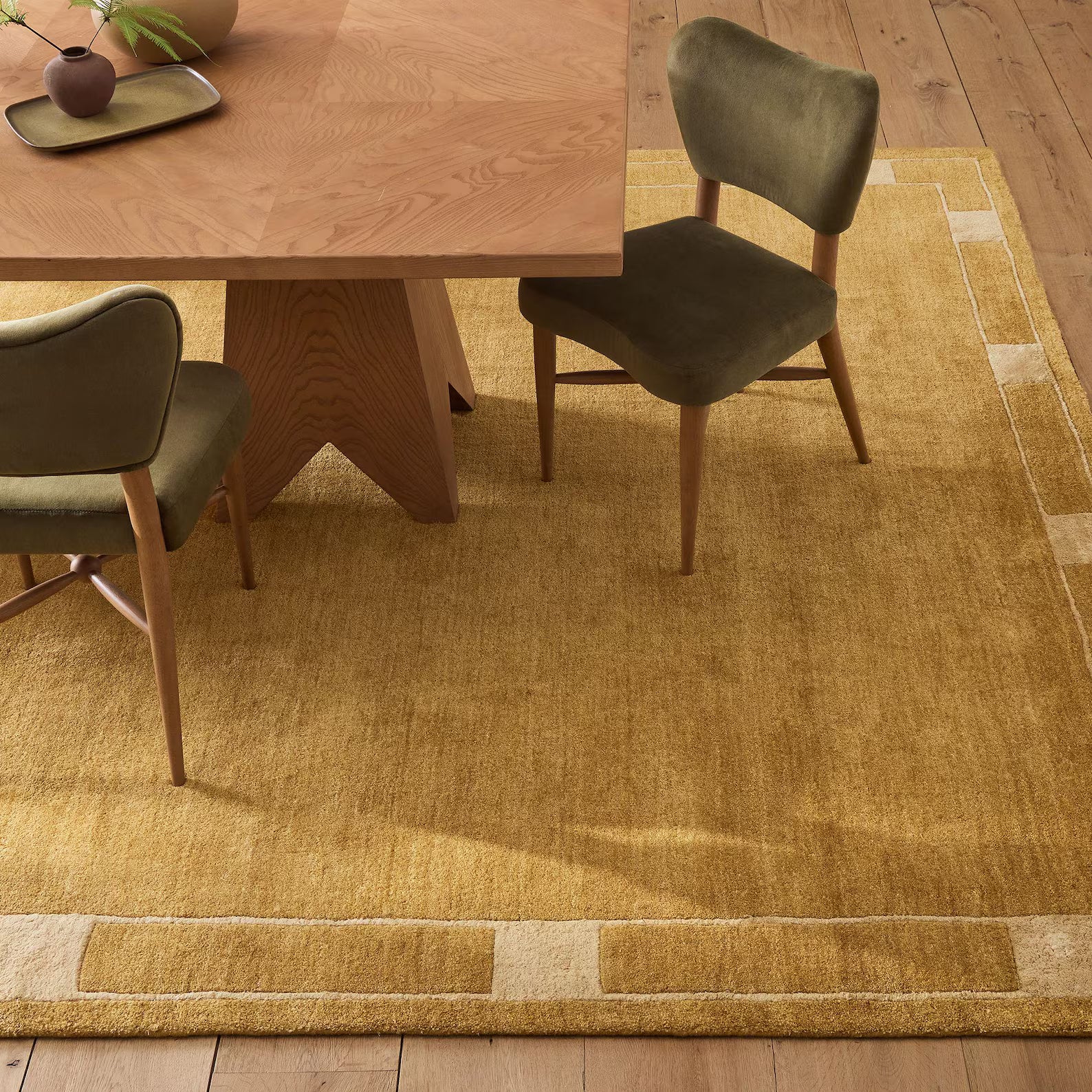 Ochre color mid-century modern hand tufted rug placed under a wooden dining table with olive green chairs in a beige and light wood interior