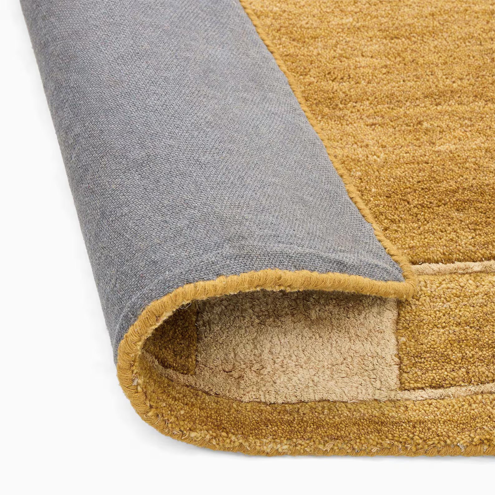 Close-up of an ochre color mid-century modern hand tufted rug with a grey underside, folded to show texture and stitched border.