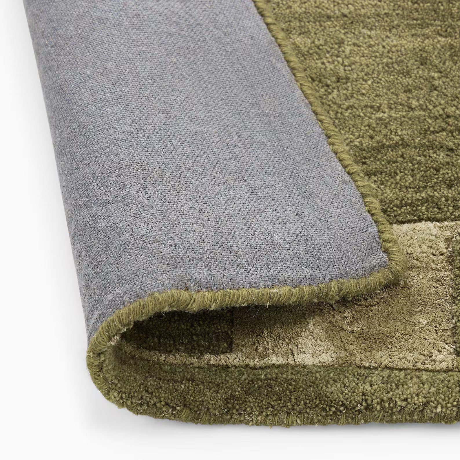 Close-up of an olive color mid-century modern hand tufted rug folded to show its grey backing and textured surface on a white background.