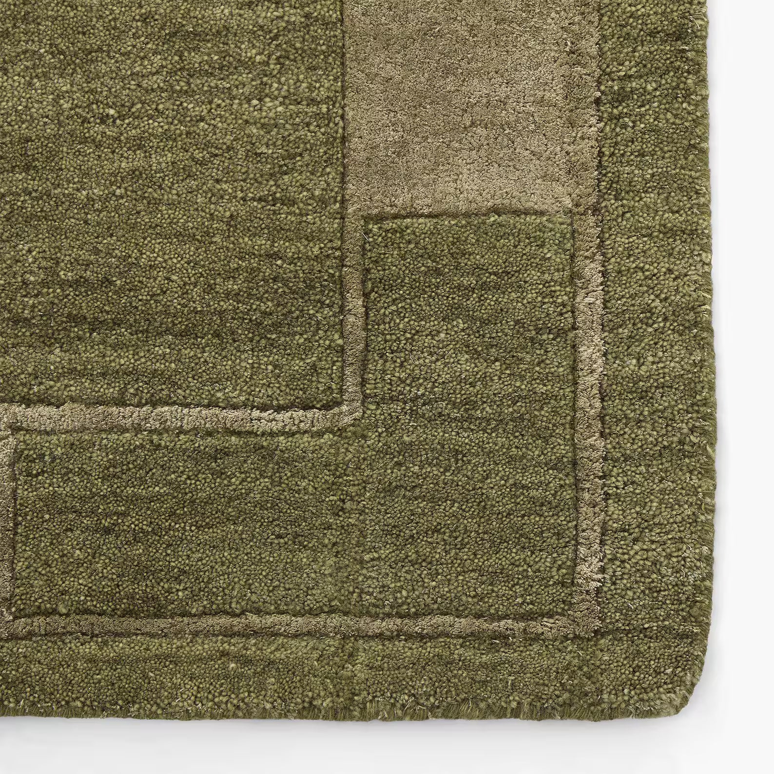 Close-up view of the olive mid-century modern rhand tufted rug corner showing tonal border detailing on a beige light-brown wooden floor.