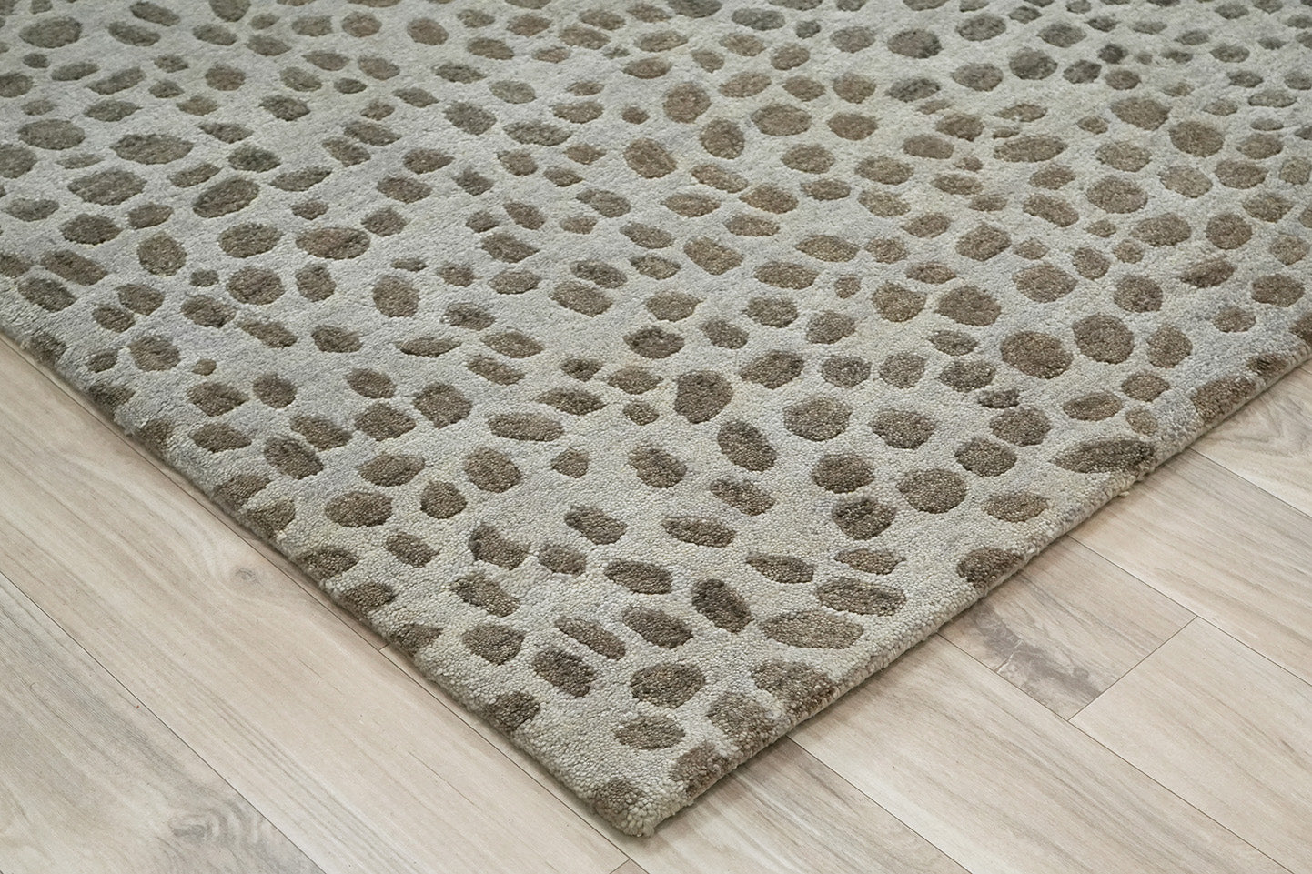 Angled corner view of Pebble Design Wool Rug hand tufted from wool showing the pebble pattern on a wooden floor 