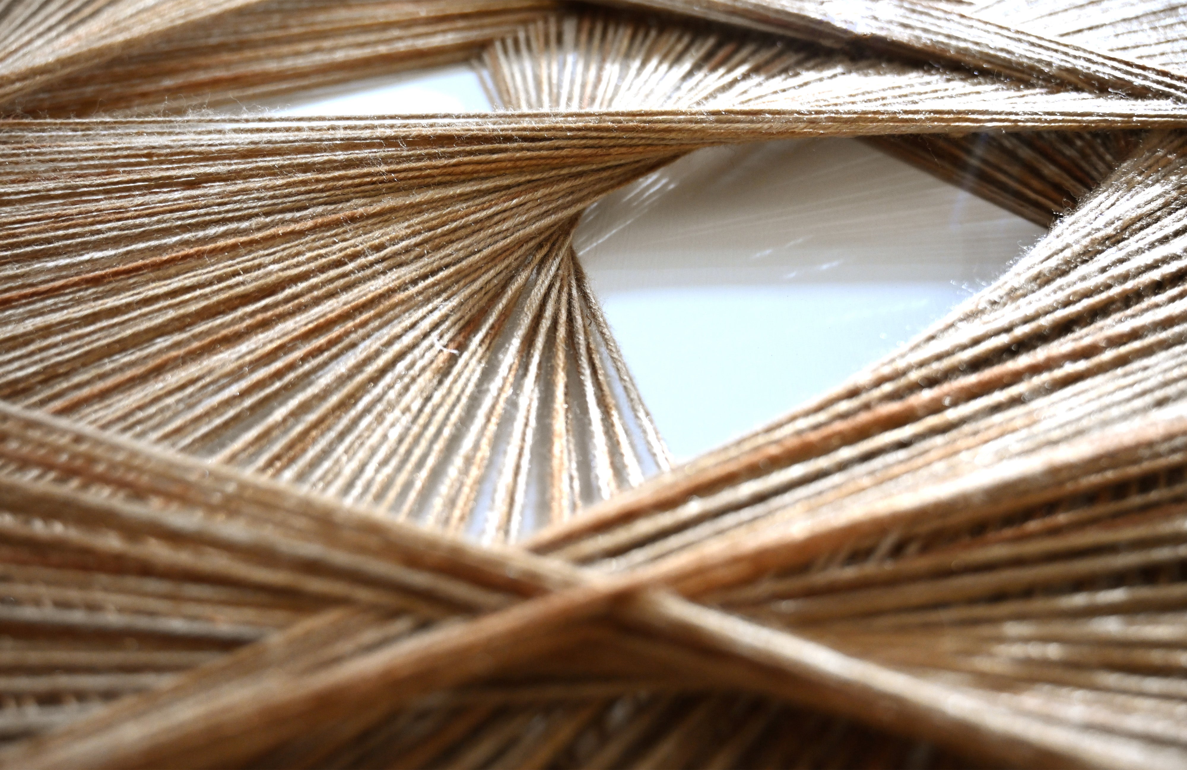 radiant axis woven wall art macro shot showing layered woven threads and central mirror detail.