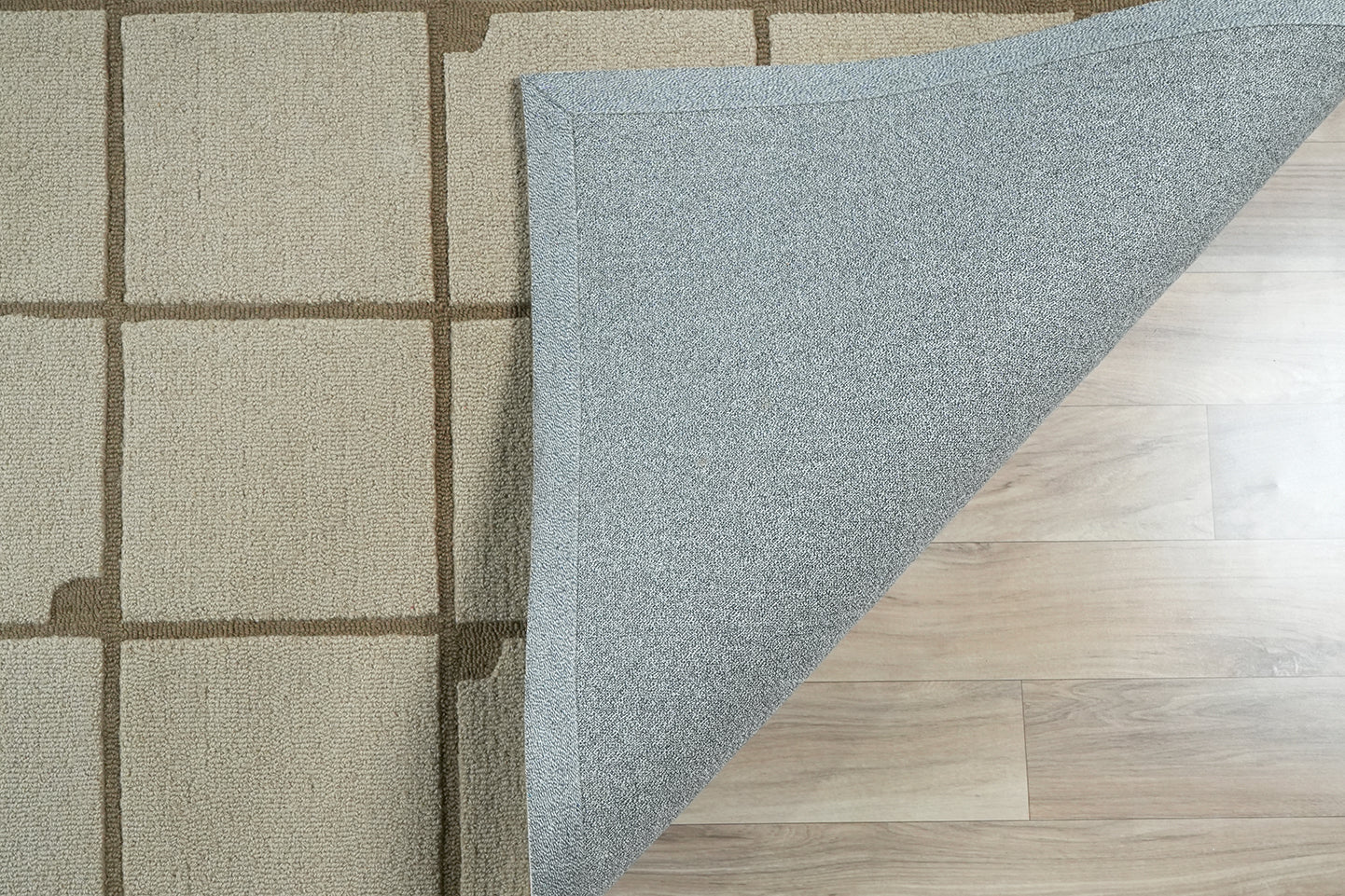 Square Field Wool Rug made from 100 % New Zealand wool with hand tufted construction showing a folded corner revealing the backing and grid structure