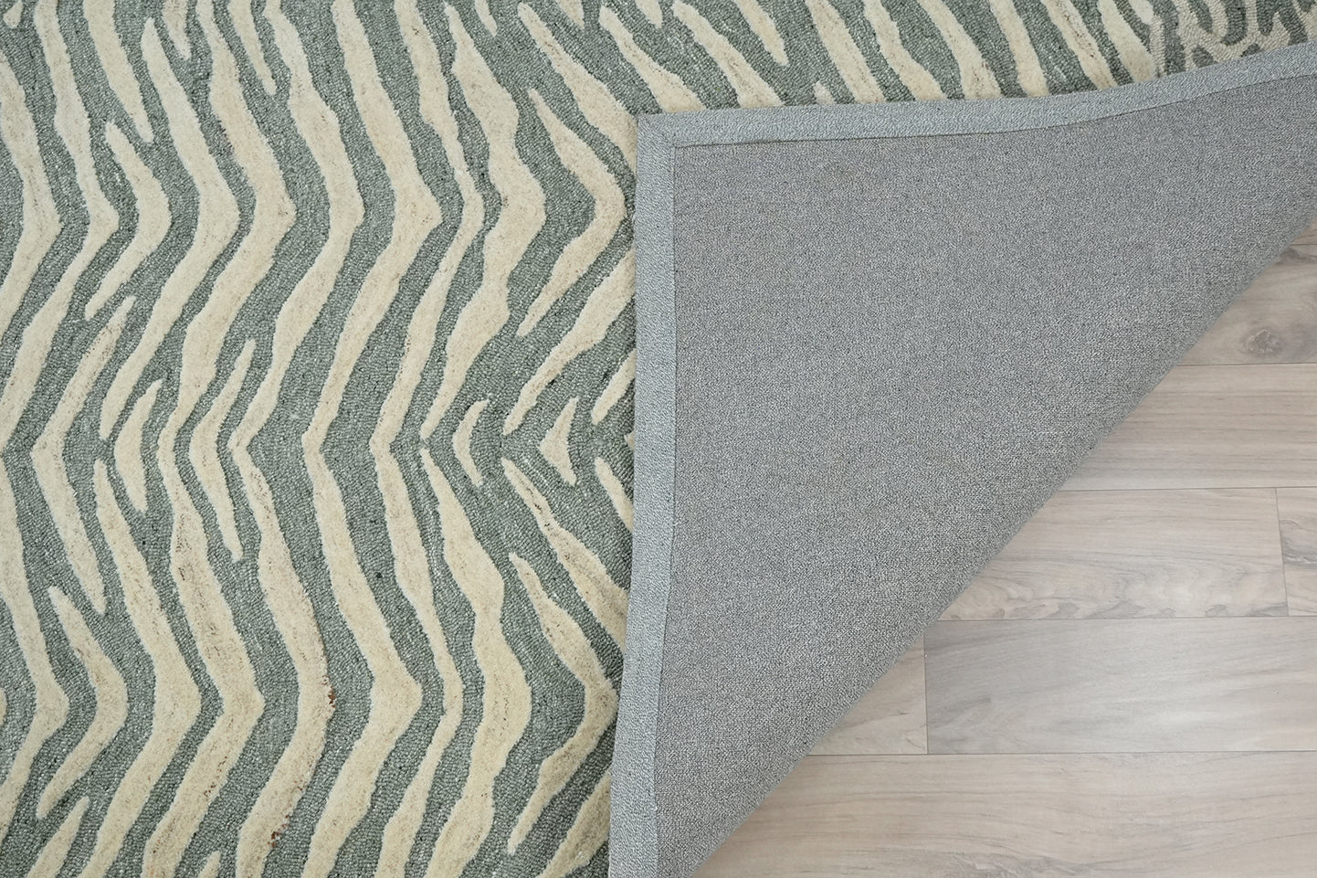 Backing view of Tide Wool Rug hand tufted from premium wool showing underside construction and edge finishing on wooden floor