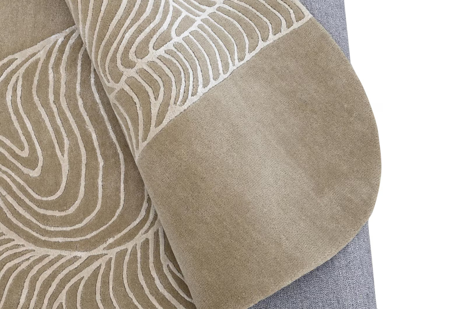 wavy abstract beige rug hand tufted with flowing white line pattern shown folded to display texture and grey backing