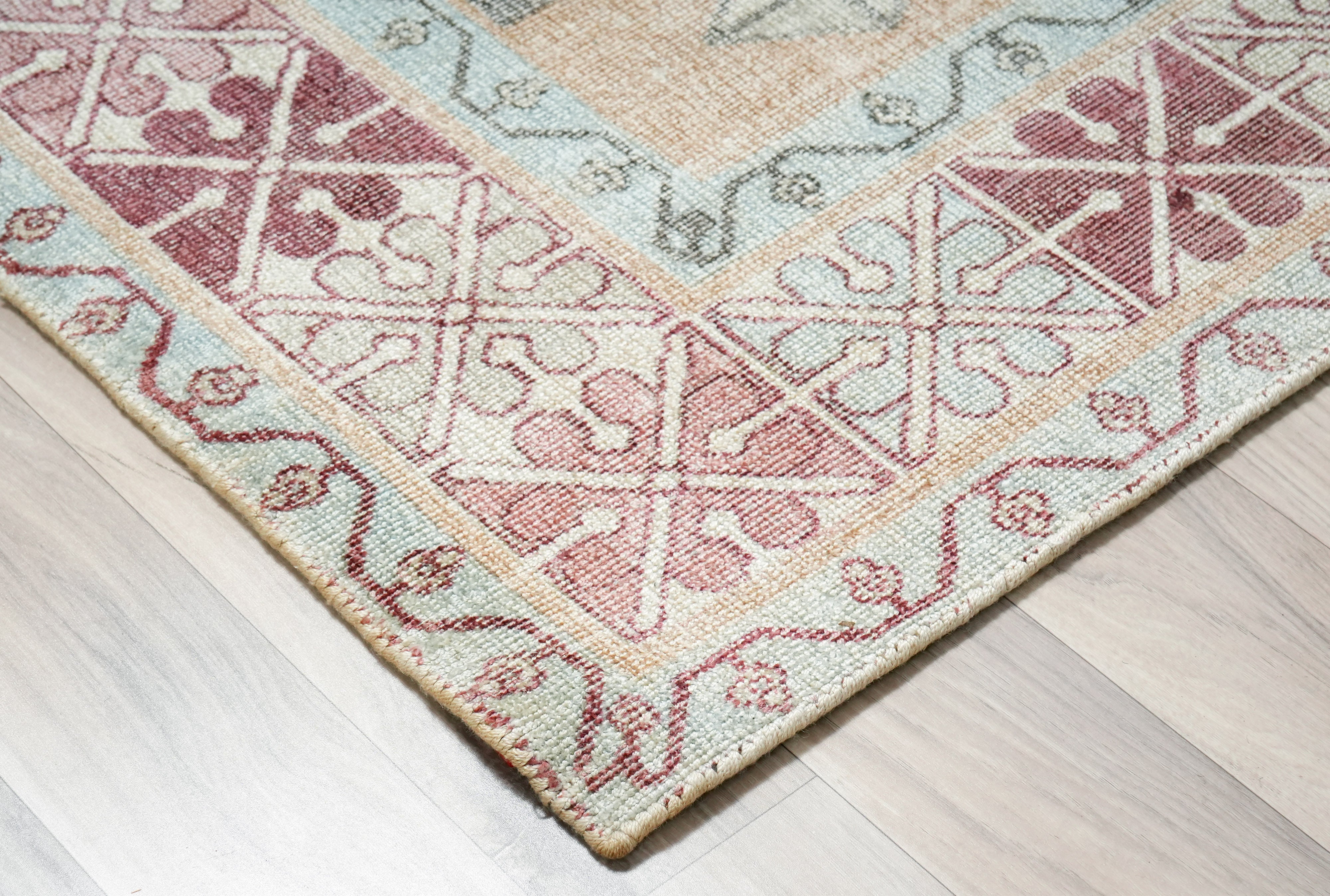 corner detail of Willowmere wool hand tufted rug showing vintage medallion pattern and wool texture in blush soft blue sand beige and ivory